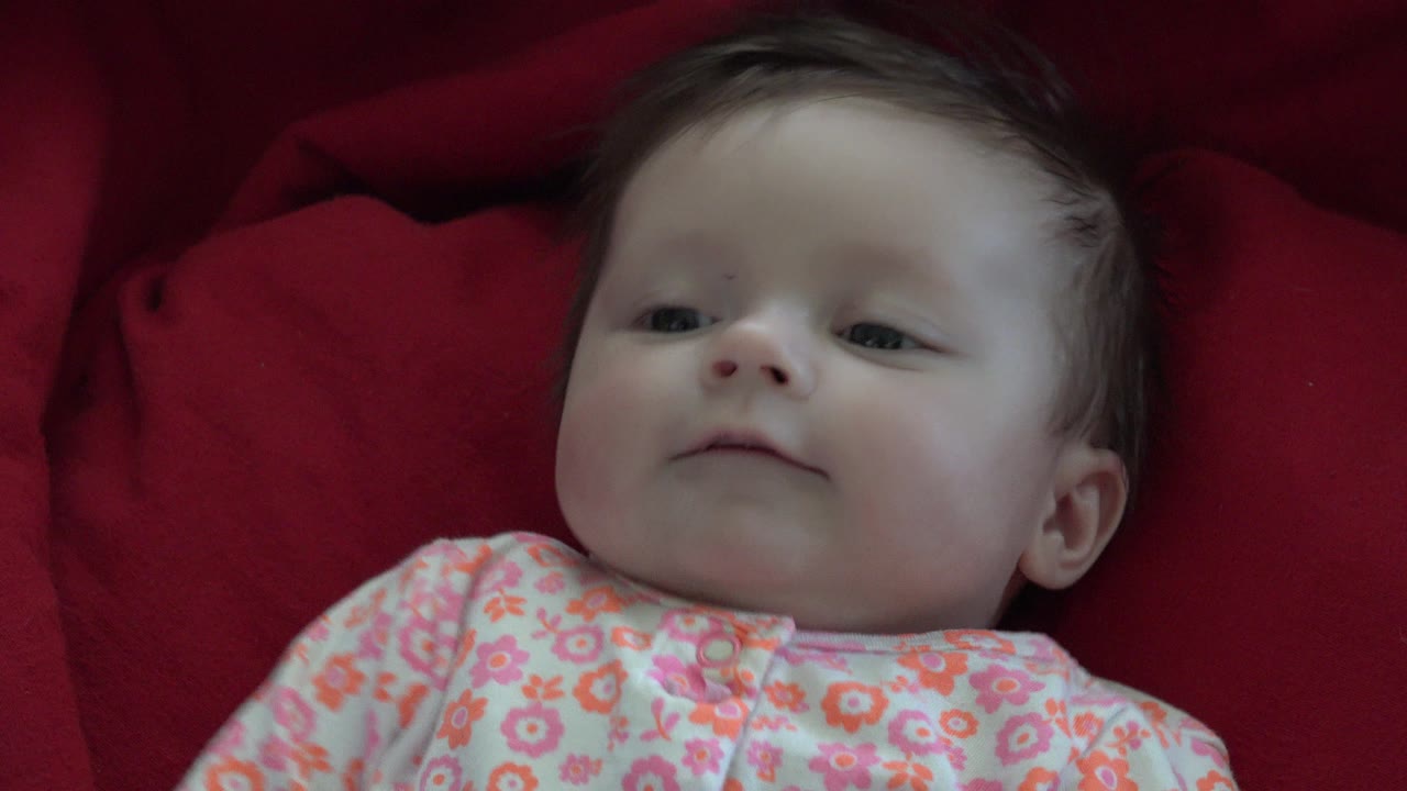 At 0:01, the infant remains close to camera on the red fabric, eyes open and face angled slightly upward in the Westminster, Colorado clip.