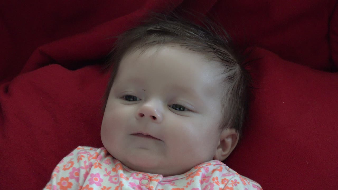 Baby lying on a red blanket in a floral outfit.