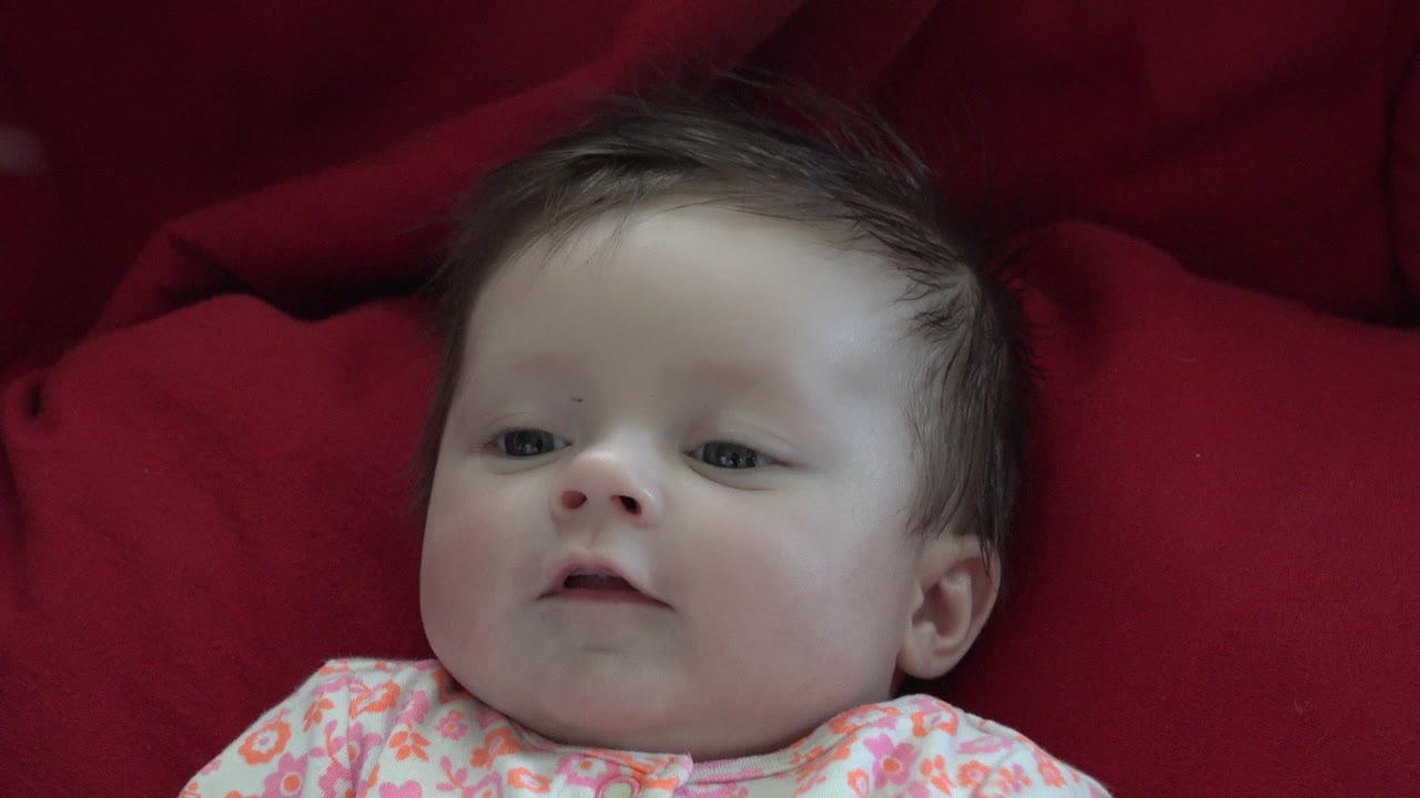 Baby lying on a red cushion in a floral outfit.