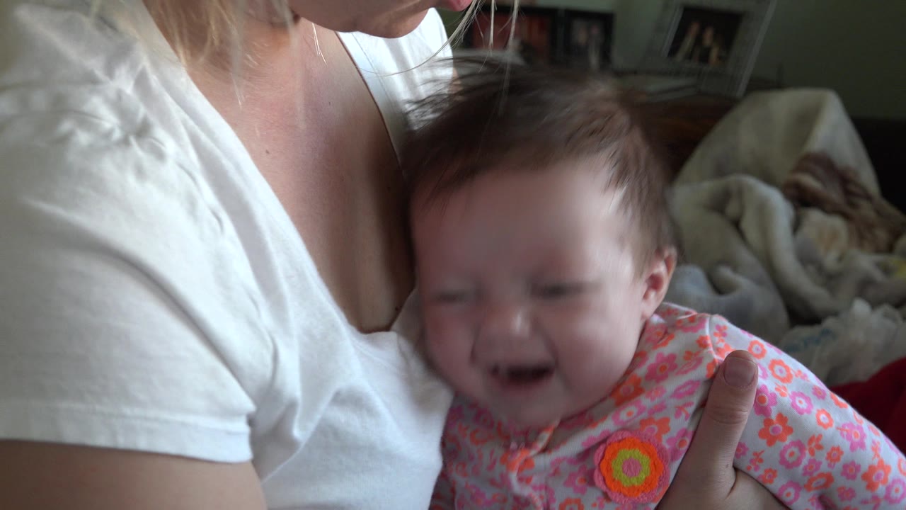 Crying infant held against an adult's chest in a living room.