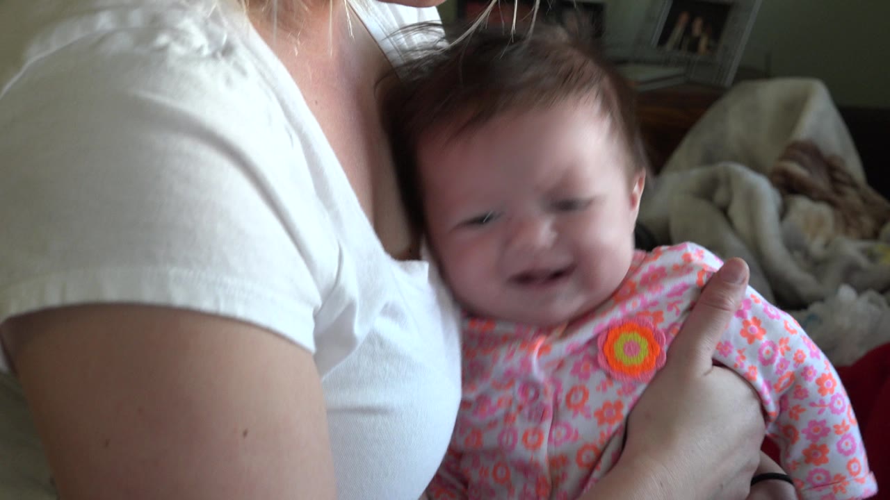 In Westminster, Colorado, the baby turns slightly outward while crying, held by an adult whose face is mostly cropped out of the close indoor frame.