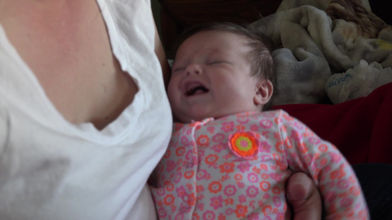 Newborn crying in a mother's lap beside a red cushion.