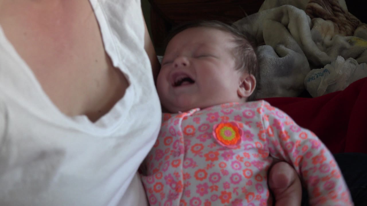 At 0:01, the newborn's face is turned upward while crying, with the mother's white shirt filling the left side of the close home frame in Westminster, Colorado.
