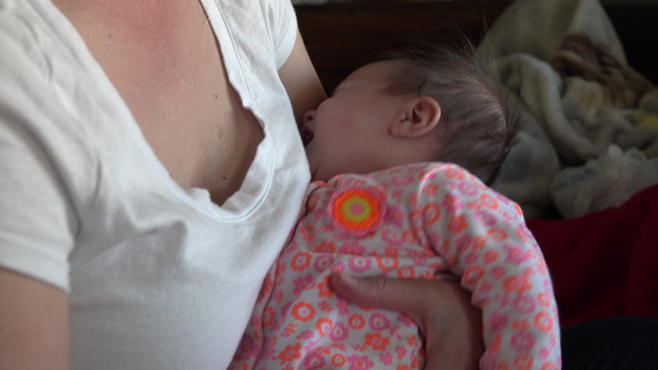 The infant remains pressed close to the woman's white shirt, with patterned clothing and soft bedding visible behind them in Westminster, Colorado.