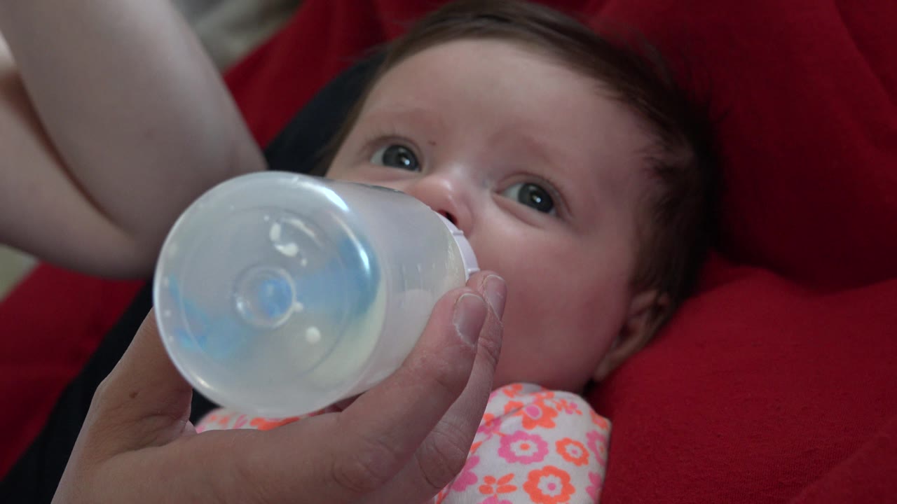 Adult hand holds a bottle to a baby's mouth.
