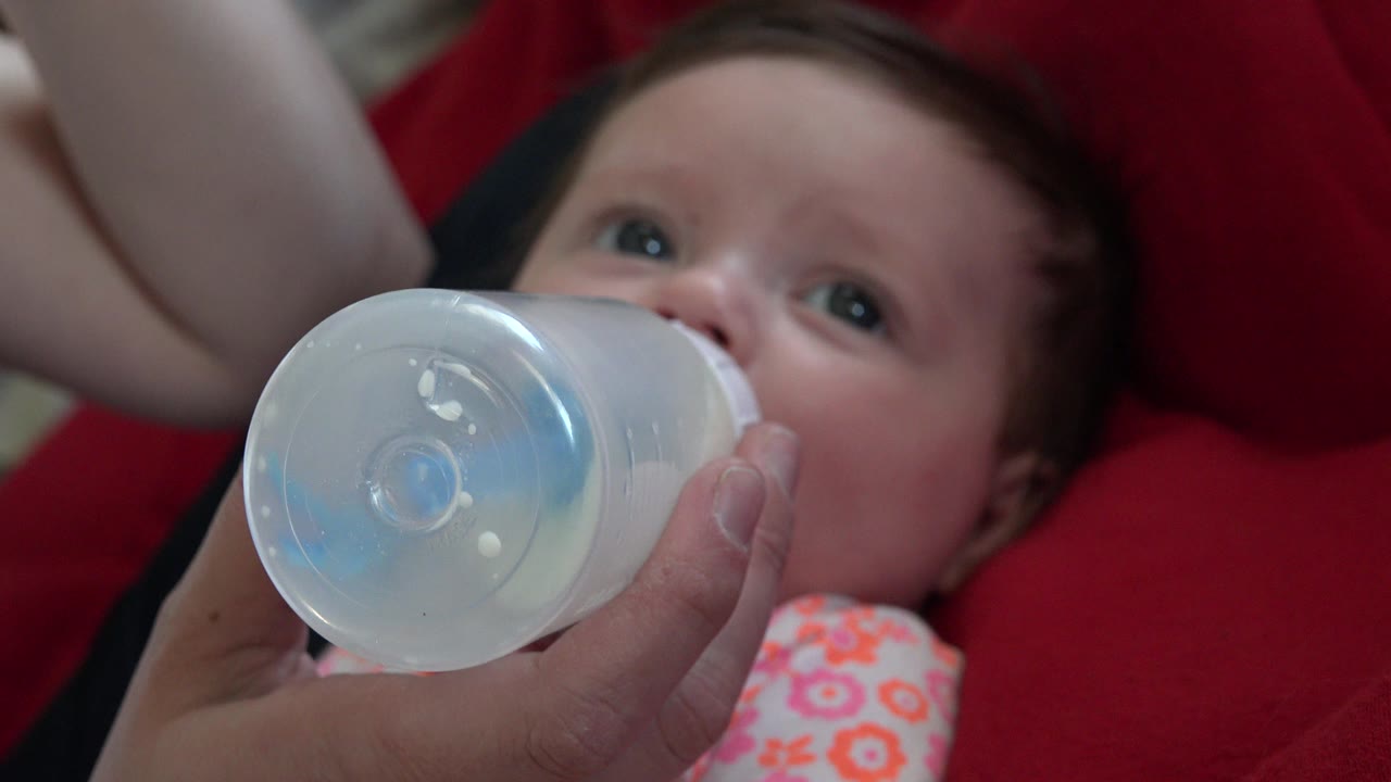 Baby drinking from a bottle held by an adult hand.