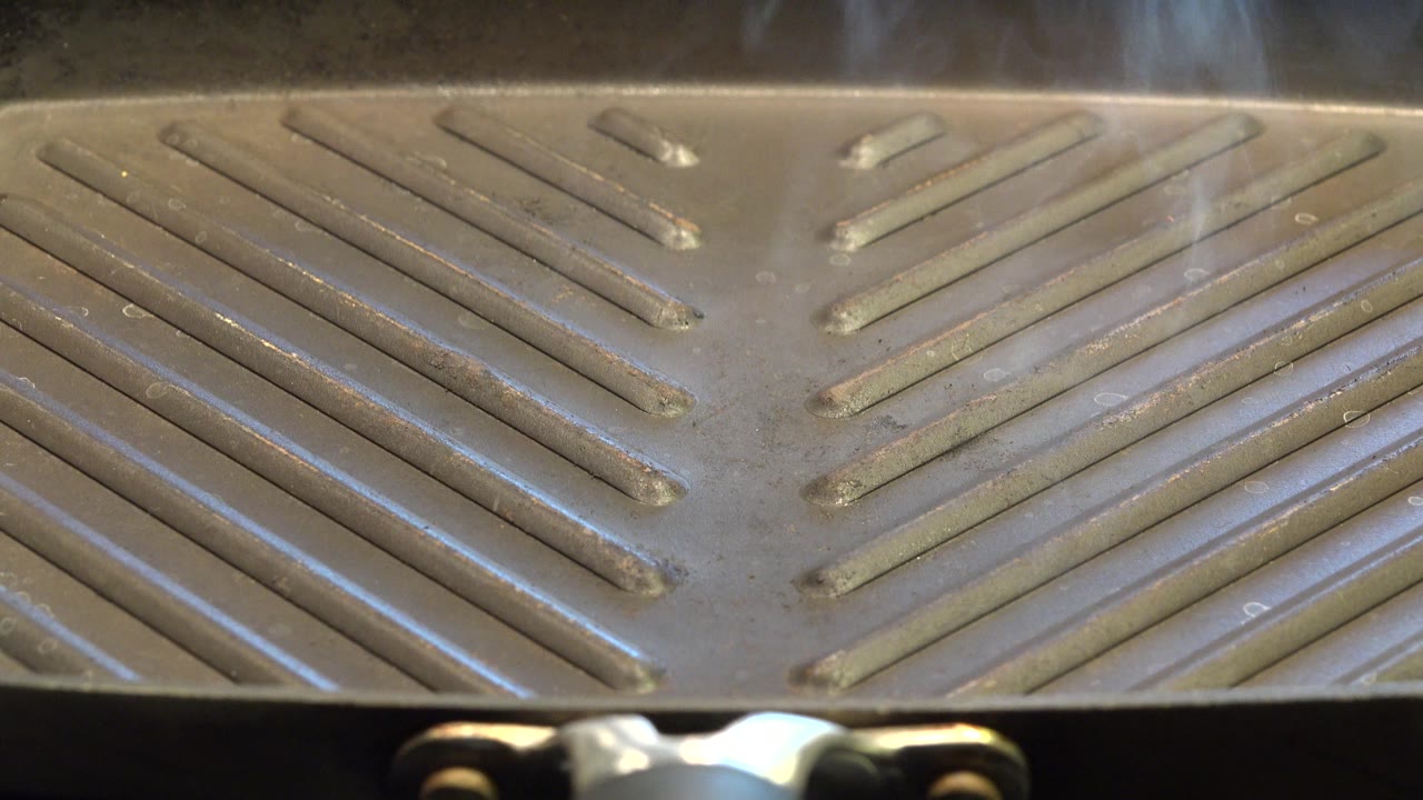 The grill surface remains tightly framed in Westminster, Colorado, with smoke hanging above the upper edge and no visible people in the frame.