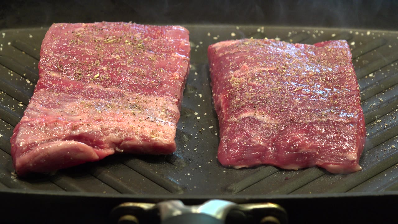 Seasoned bacon pieces cooking on a dark pan with light steam.