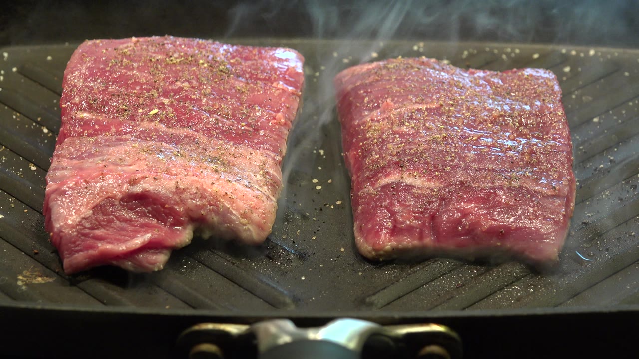 The beef pieces remain centered on the ridged grill pan in Westminster, Colorado, with seasoning across the meat and thin steam above, no visible people.