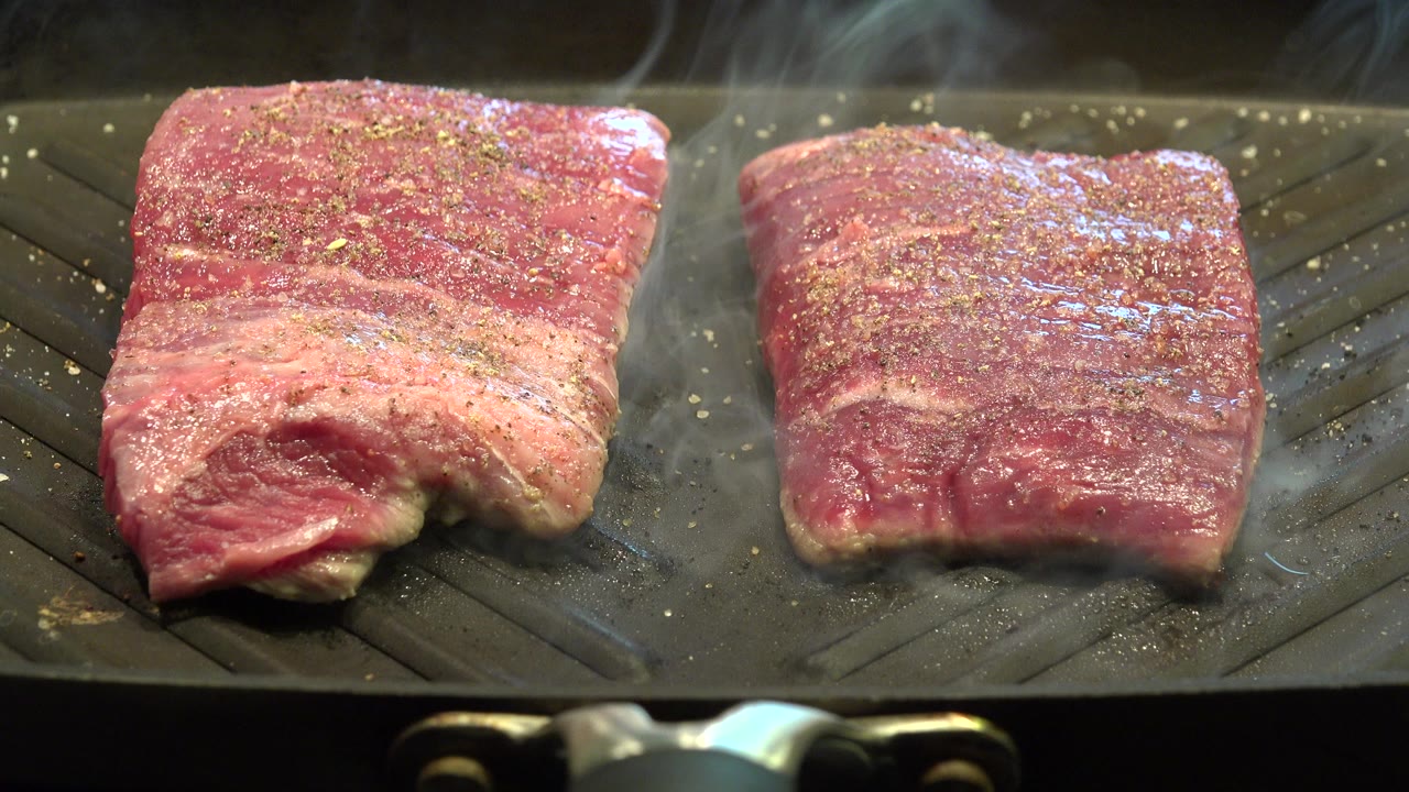 Two seasoned skirt steaks rest on a gray indoor grill in Westminster, Colorado, with steam rising and no visible people.