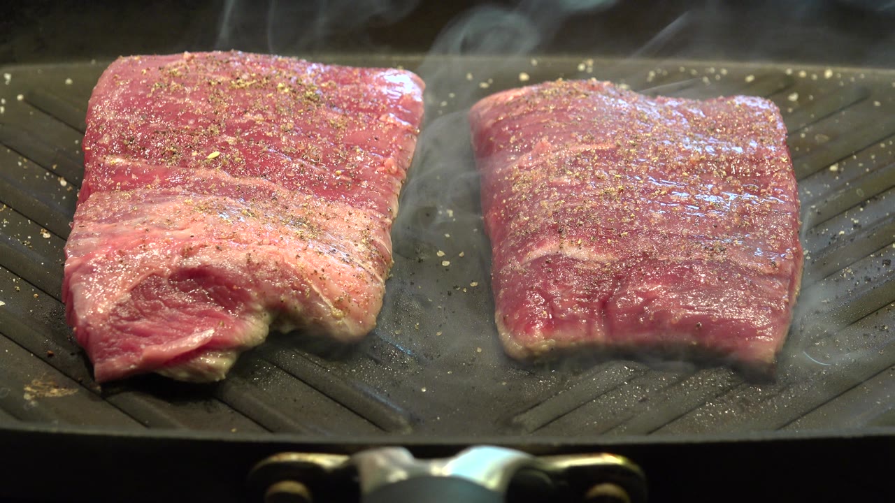 Close-up of two steaks cooking on a ridged grill