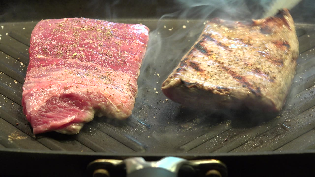 At 0:00 in Westminster, Colorado, two pieces of seasoned meat sit on a ridged grill pan, one red and one browned with grill marks, with smoke rising and no visible people.