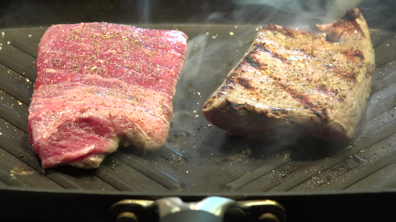At 0:01 in Westminster, Colorado, the raw red meat remains on the left while the browned piece on the right shows dark grill marks under drifting smoke, with no visible people.