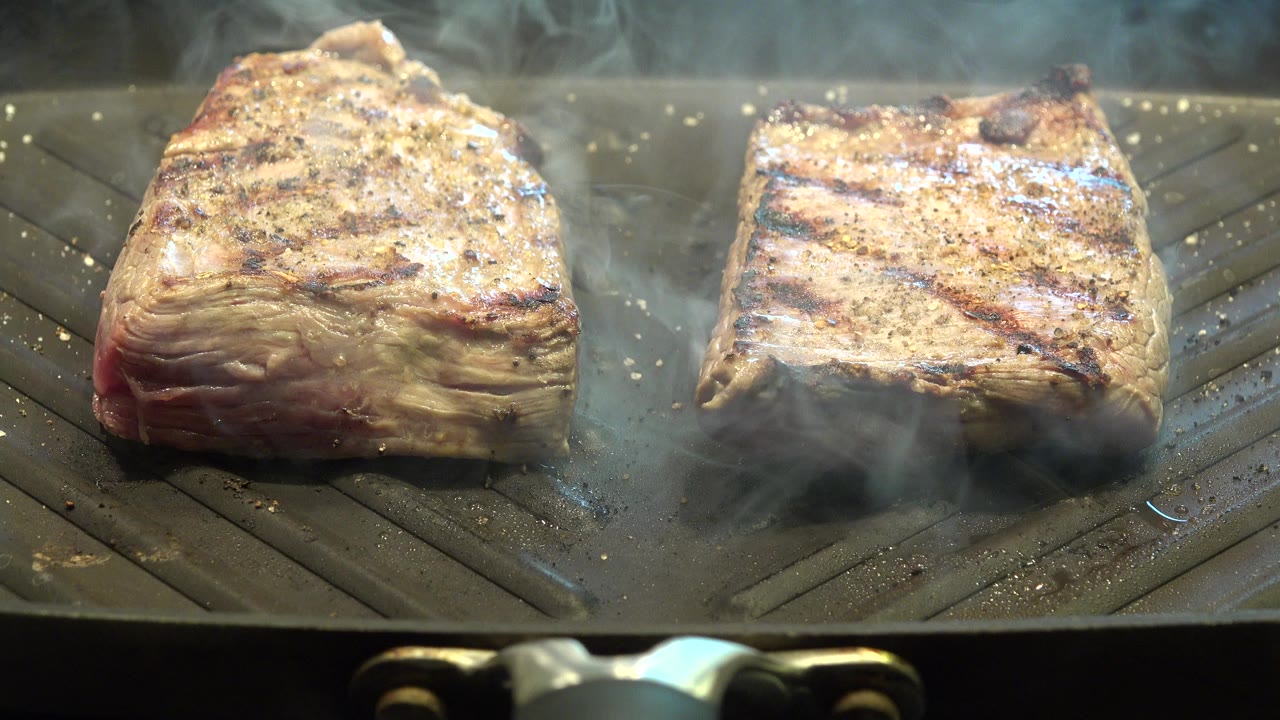 Two seasoned steaks smoking on a gray indoor grill.