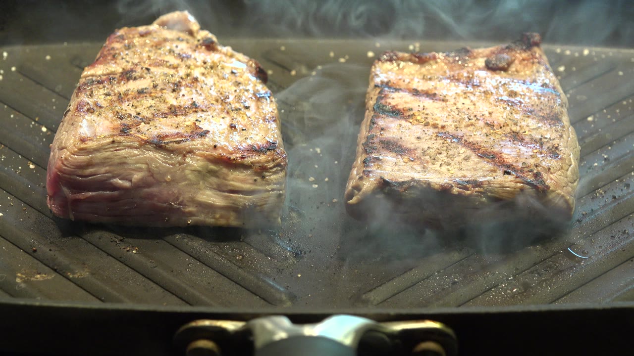 Two seasoned meat pieces smoking on a ridged grill.