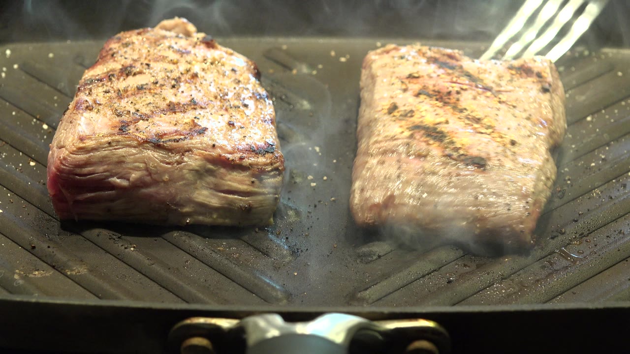 Two pieces of meat brown on a ridged flat grill in Westminster, Colorado, with steam rising and no visible people.