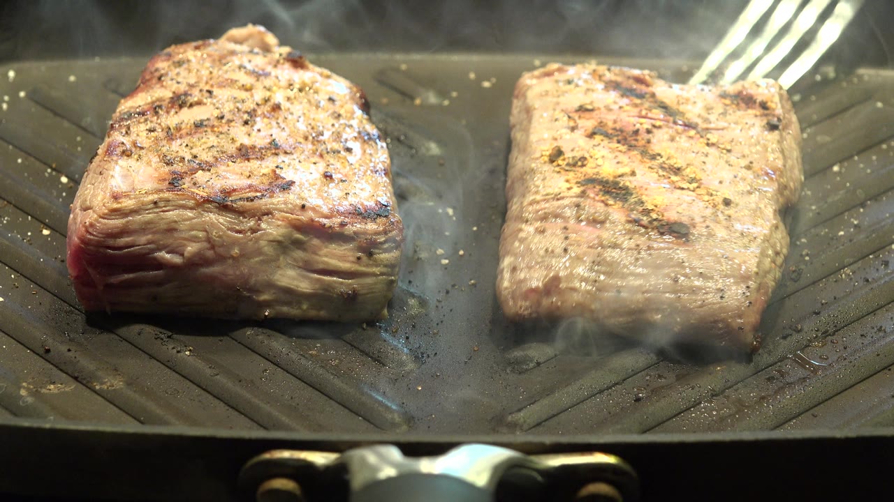 A metal fork or tongs reaches toward the right piece of meat on the smoking ridged grill in Westminster, Colorado, with no visible people.