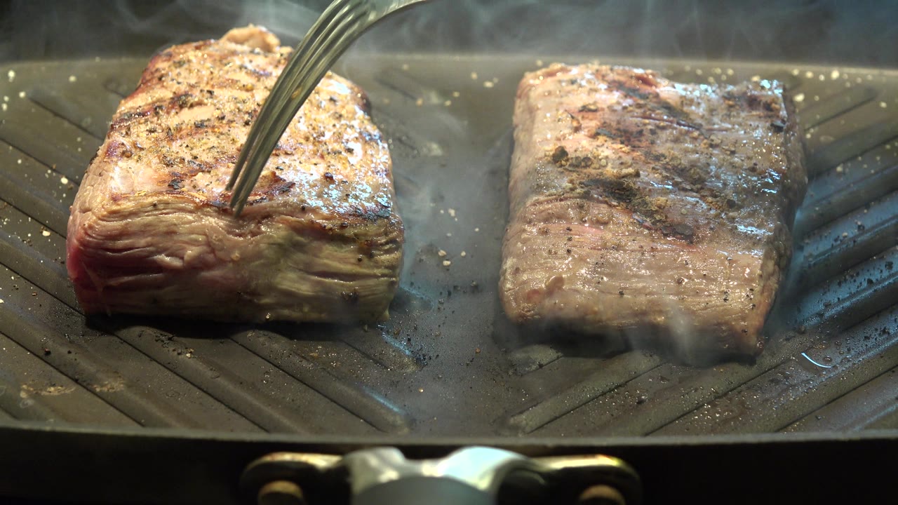 Utensil presses into browned meat beside another grilled piece.