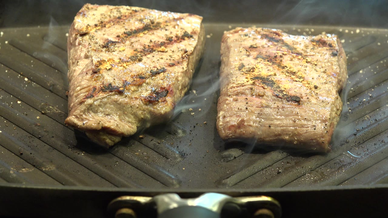 At 0:01, the meat remains centered on the ridged grill pan in Westminster, Colorado, with smoke lifting behind the left piece and no visible people.