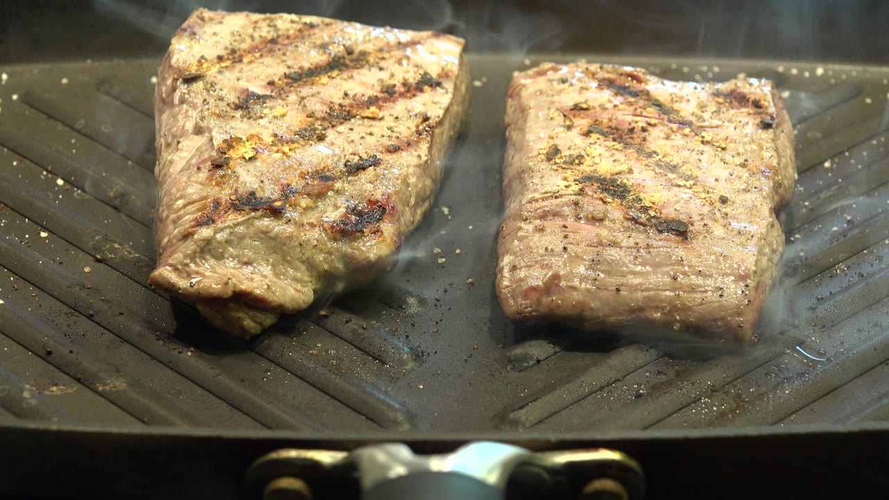 Two seared meat pieces cooking on a dark grill pan.