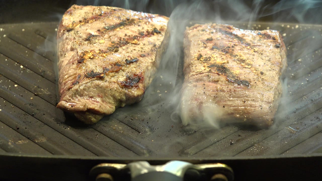 Two steaks smoking on a ridged grill pan.