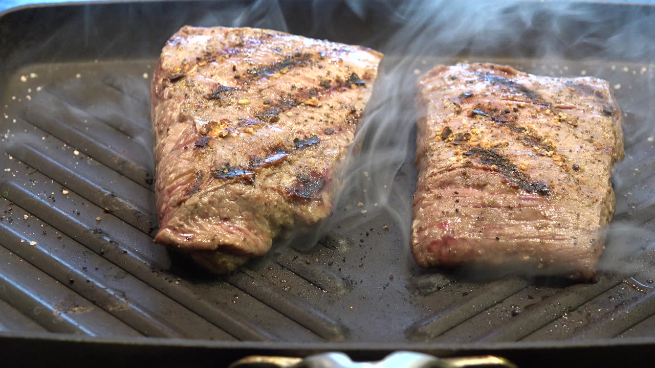 Smoke thickens between two pieces of browned meat on the fryer pan, with charred grill marks and no visible people.