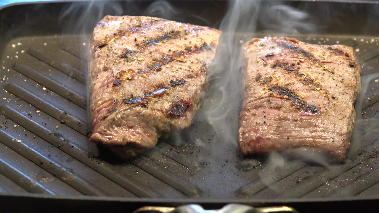 Two steaks smoking on a ridged indoor grill pan.