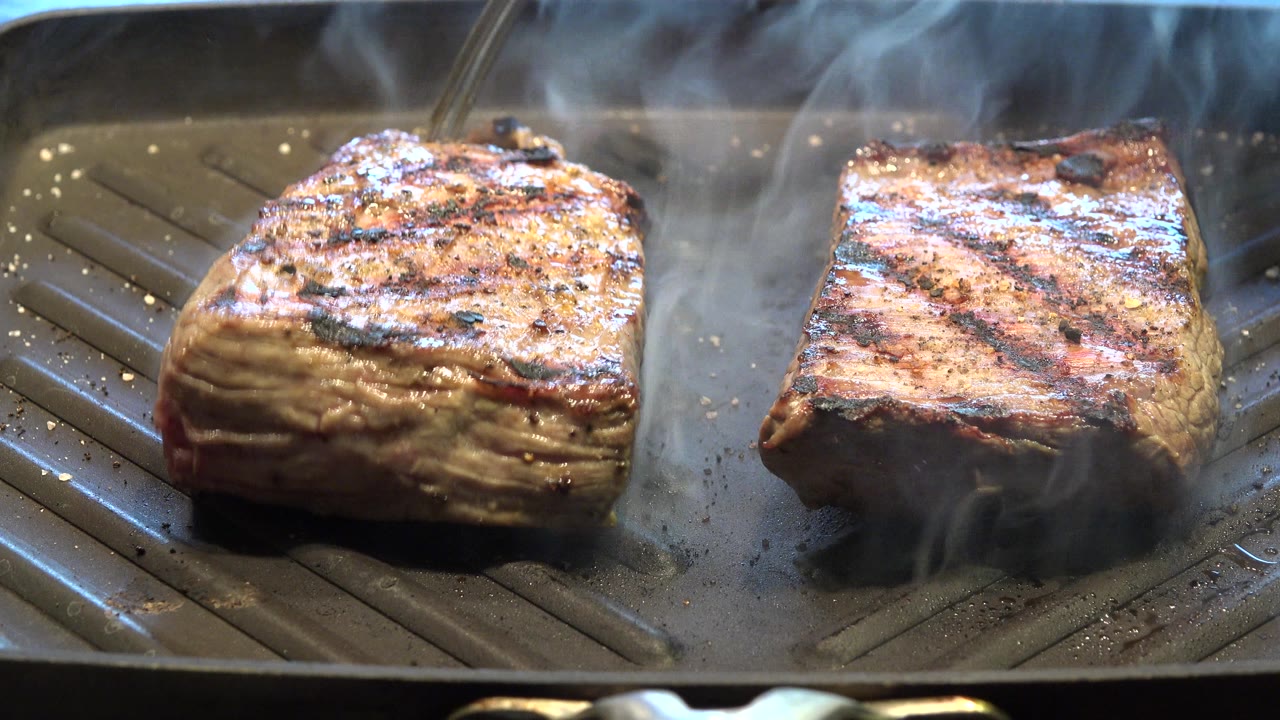 Two pieces of grilled meat on a ridged pan with steam.