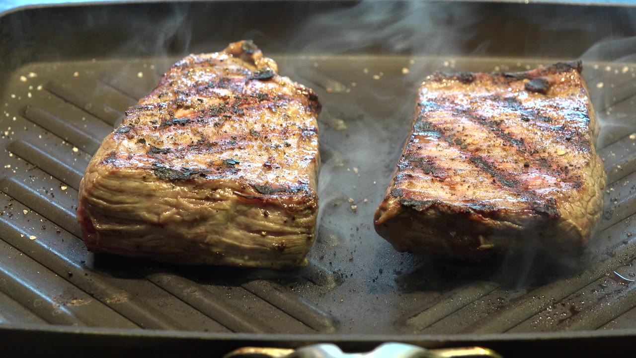 Two pieces of meat smoking on a ridged grill pan.