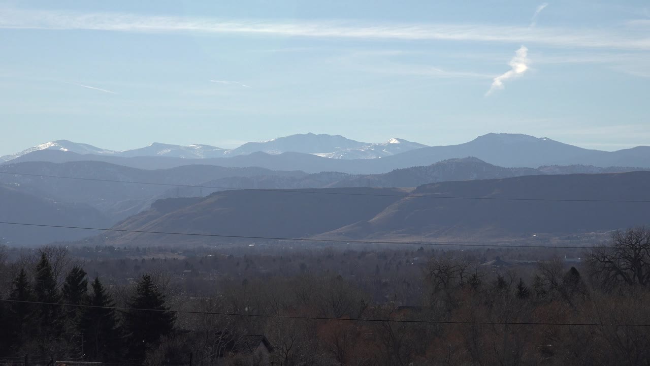Snow-dusted mountain horizon above hazy foothills and bare trees.