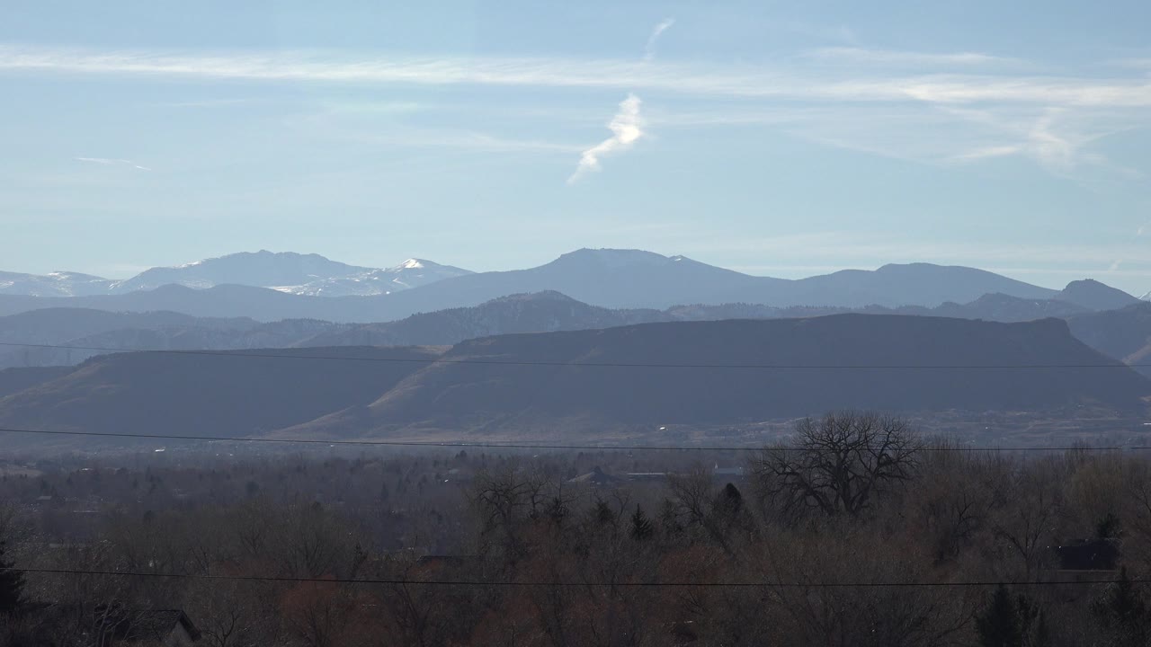 Distant mountains beneath blue sky with bare trees in the foreground