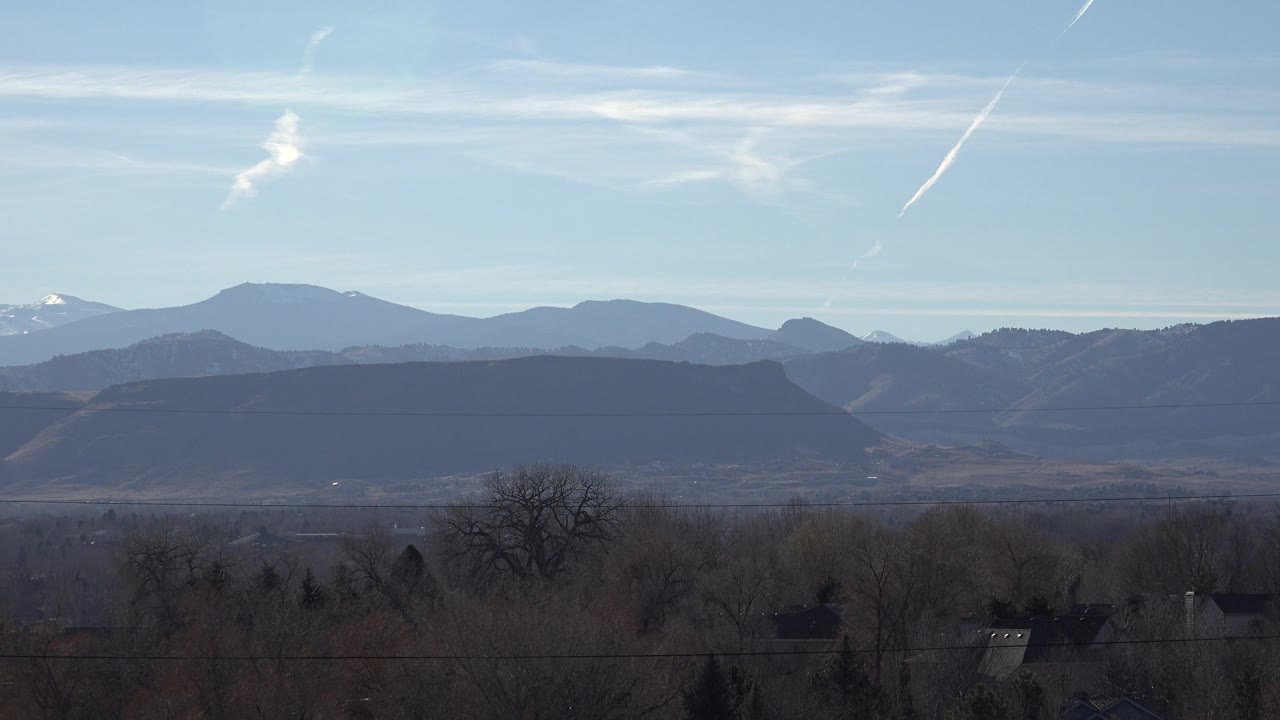 Snow-tipped distant peak behind darker mountain ridges and trees.