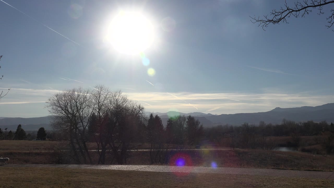 Bright sun over open grass, bare trees, and distant mountains with no visible people.