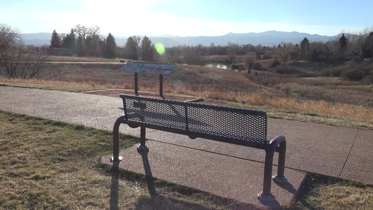 Black metal bench facing a path and distant mountains under bright sky.