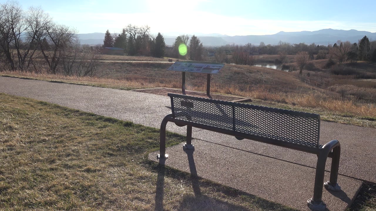 Park bench beside a paved path with an information board and distant hills.