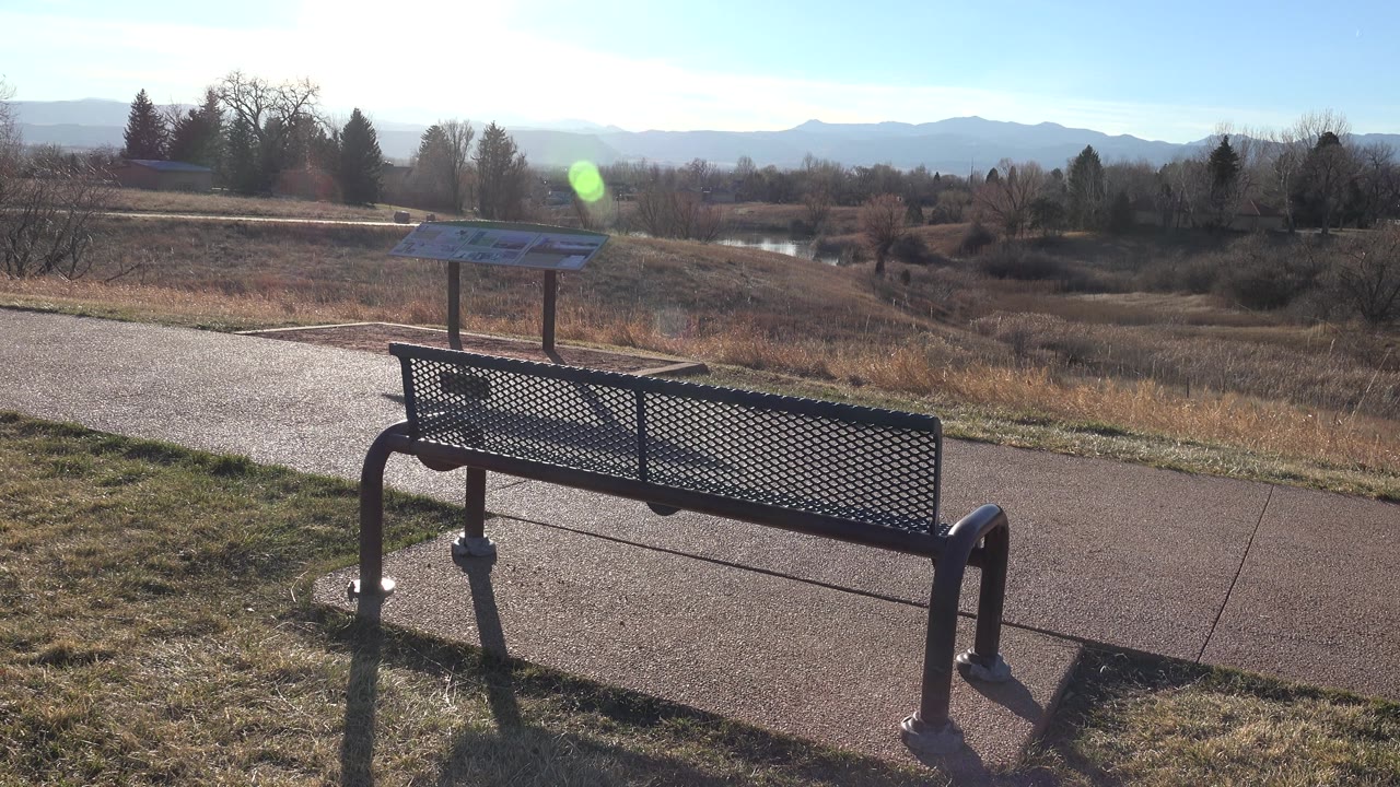 Bench in front of an interpretive sign with a paved path and open reserve beyond.