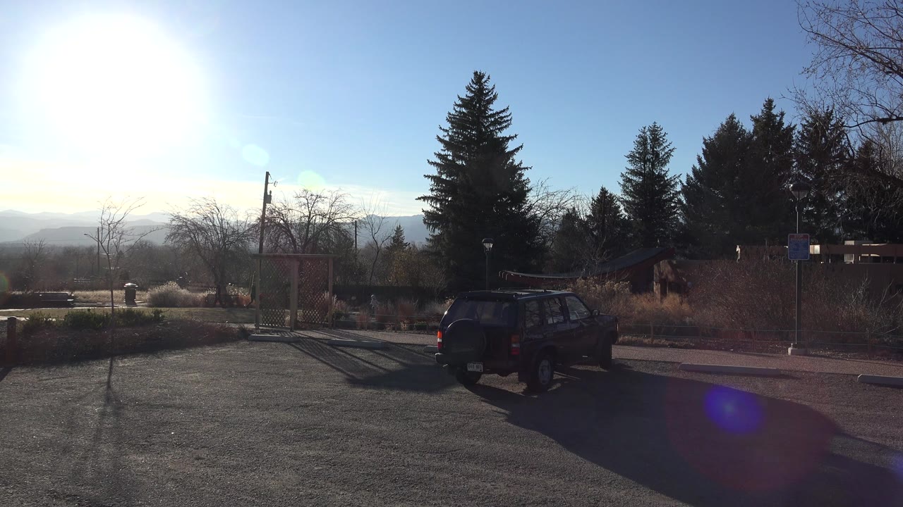 One second into the Arvada, Colorado park clip, the dark SUV remains near the paved edge while the playground frame, evergreens, bare branches, hazy hills, and no visible people fill the background.