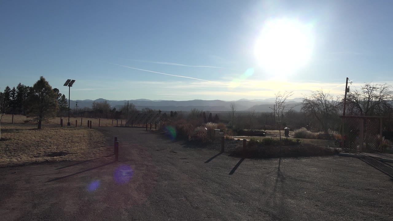 Frosty field, trees, solar light pole, and distant hills beneath a bright sky.