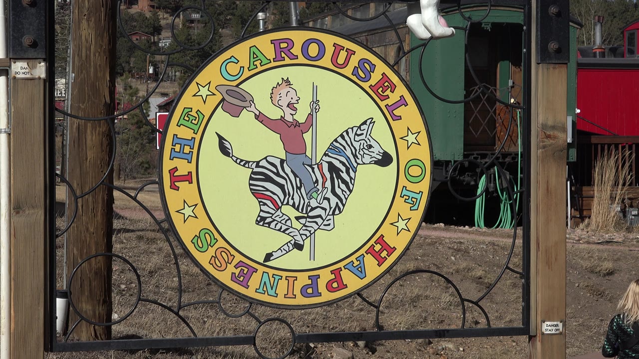 Large Carousel of Happiness sign beside wood posts and black metal fencing.