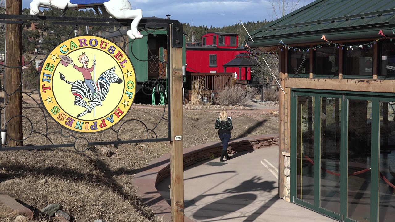 Nederland, Colorado frame with the woman and child slightly farther down the paved path, the yellow carousel sign at left, and the green building filling the right side.