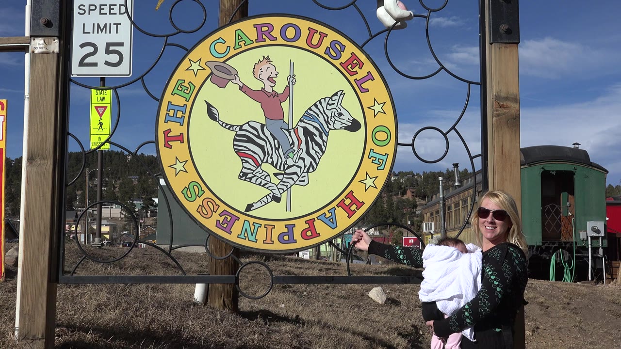 Woman holding a child beside a yellow Carousel of Happiness sign.