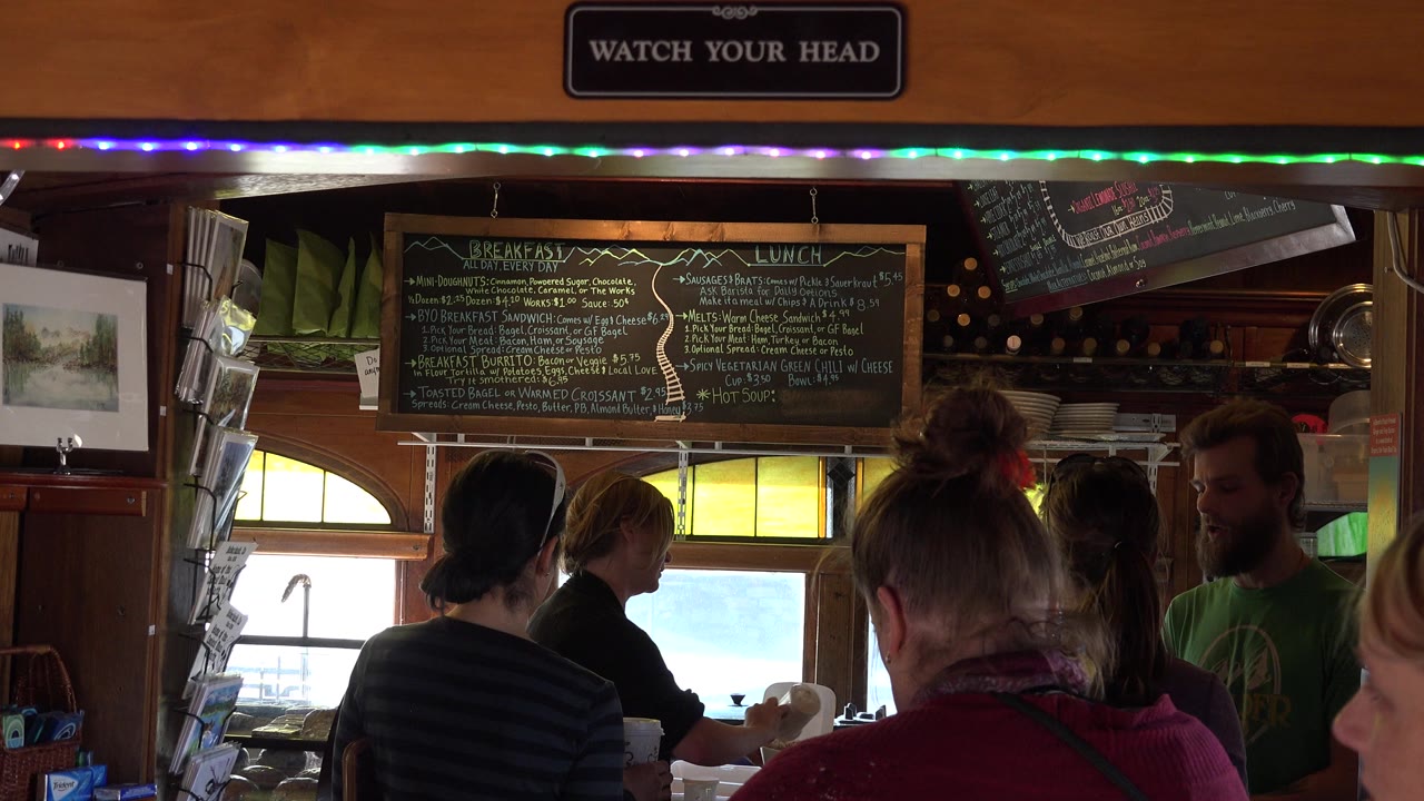 In Nederland, Colorado, the line remains clustered in the foreground while a chalkboard menu, arched windows, and colored string lights frame the service area.