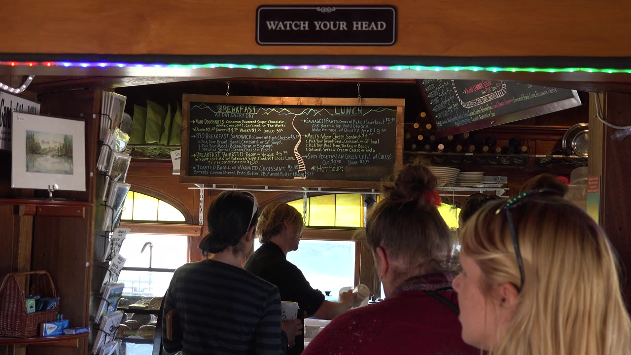 A blonde woman enters the right foreground as people wait near the counter.