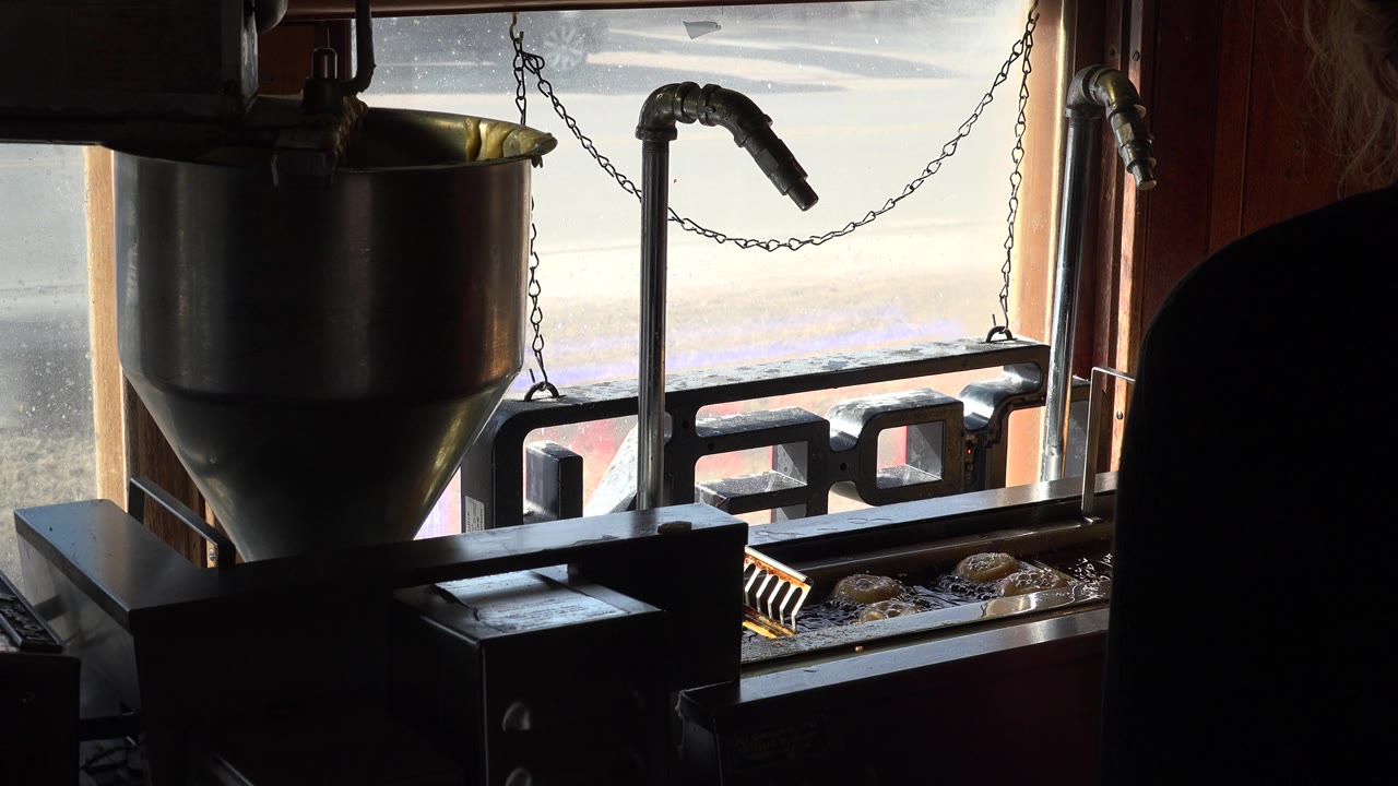 Backlit fryer or doughnut-making equipment sits beside a bright window in Nederland, Colorado, with small fried items visible below and no clear face visible.