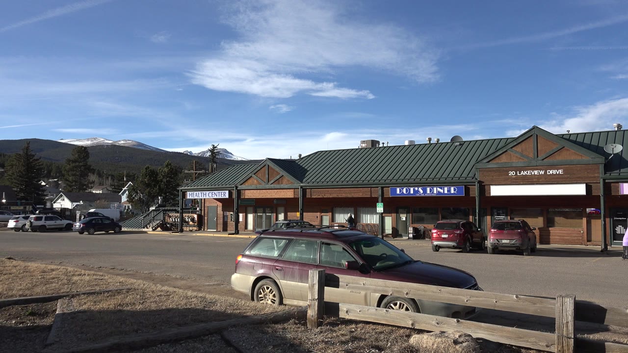 Roadside strip mall with parked cars and mountains behind it.