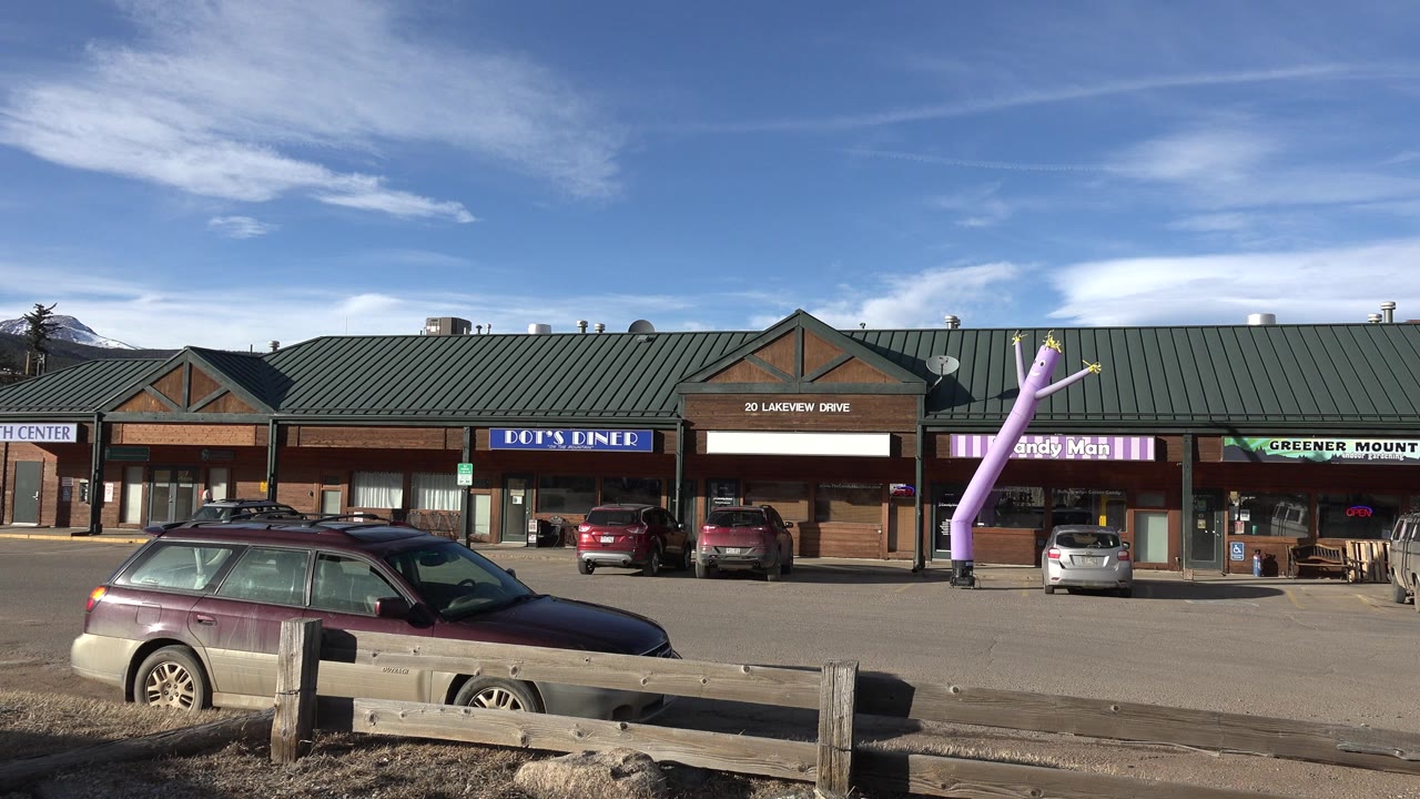 Brick shopping center with parked cars and a purple inflatable figure