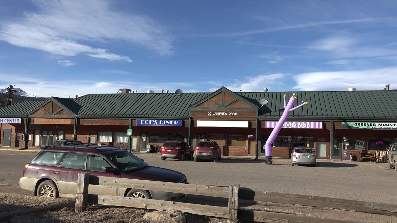 Second frame shows the Nederland, Colorado storefront row from across the parking area, with the purple inflatable figure closer to center and no visible people.