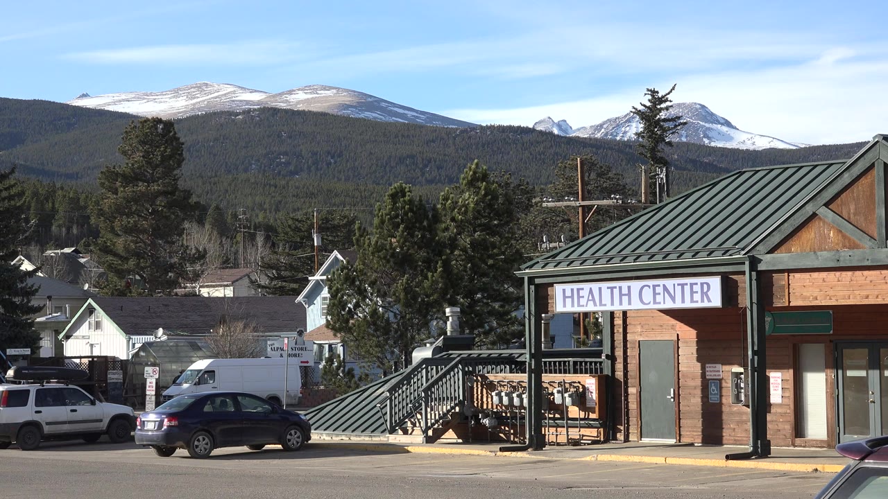 Health Center building with parked cars and snowy mountains behind it