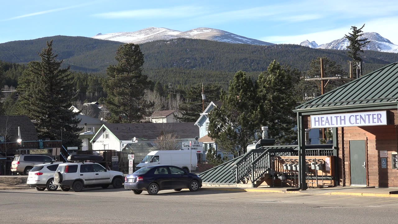 Roadside Health Center building with parked cars and mountains behind it.