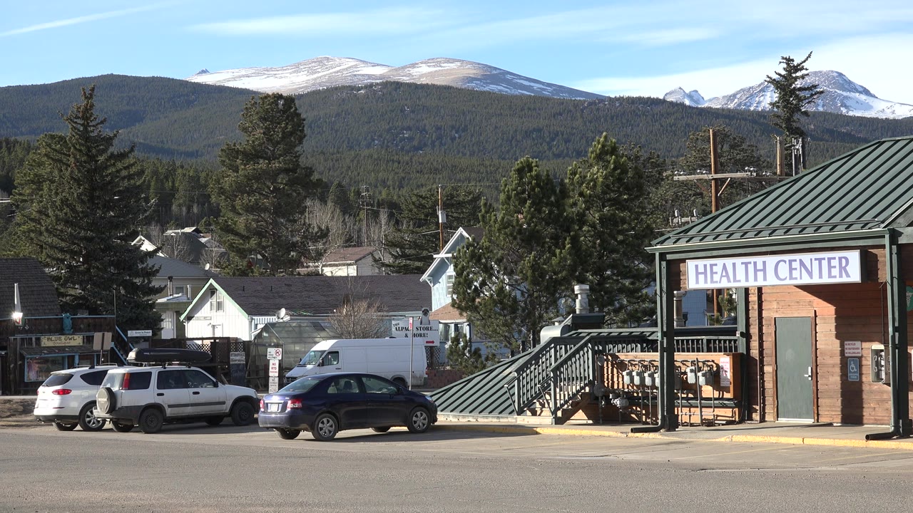 Health center building beside parked cars with mountains behind it.